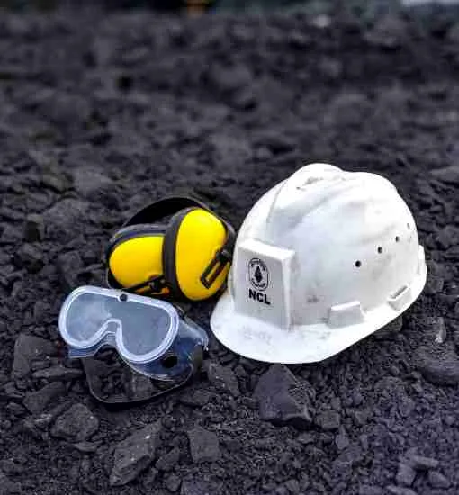 Safety goggles, ear protection and a hard hat resting on coal at a mine site